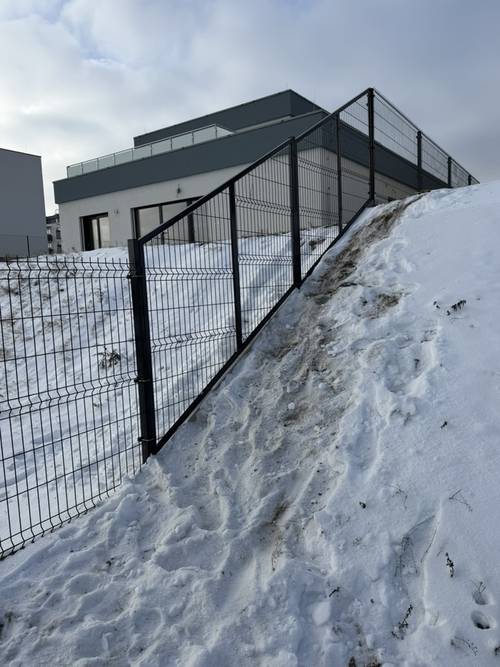 Branka v plotu z černých 3D panelů vedeném ve svahu